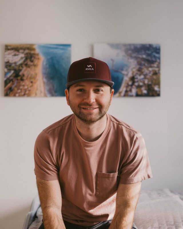 Andrew smiling in front of two of his aerial coastline prints