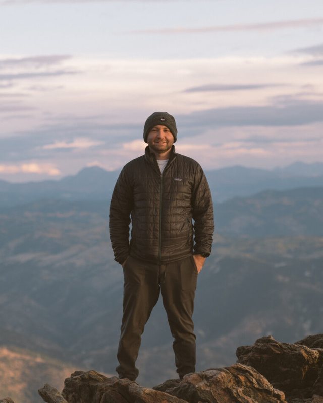 Andrew standing on a rocky summit above mountain ridges at dusk